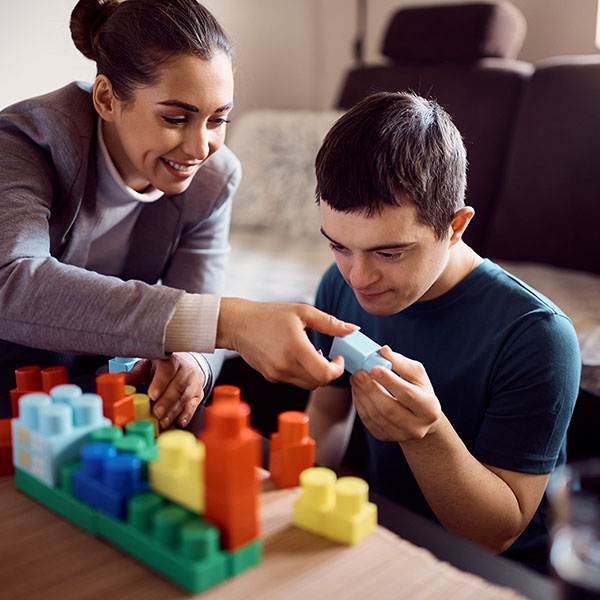 Man with down syndrome enjoys while stacking toy blocks with his psychologist at home.